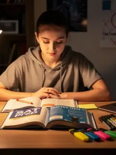Estudiante concentrada en la preparación del examen SAT con libros y laptop, planificando su estudio intensivo de 3 meses.